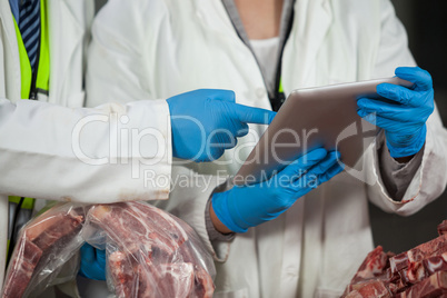 Technician using digital tablet while examining meat