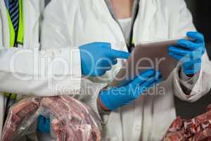 Technician using digital tablet while examining meat
