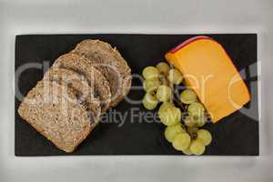 Slices of brown bread, grapes and gouda cheese on slate board