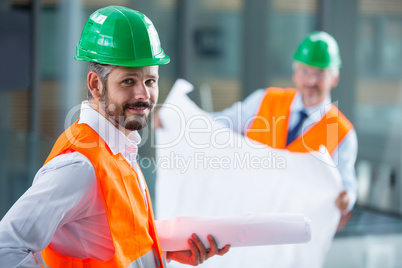 Architect in hard hat standing with blueprint in office corridor