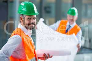 Architect in hard hat standing with blueprint in office corridor