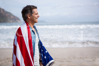 Man wrapped in amrican flag standing on beach
