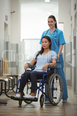 Female nurse assisting patient on wheelchair in corridor