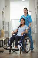 Female nurse assisting patient on wheelchair in corridor