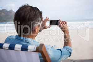 Rear view of man taking picture on mobile phone at beach