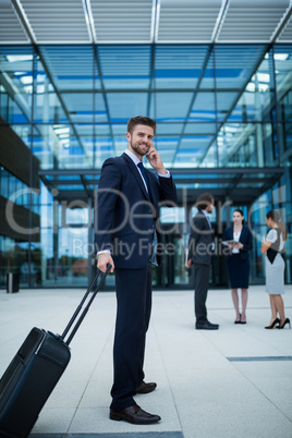 Businessman holding suitcase talking on mobile phone