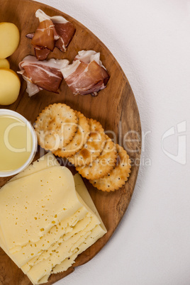 Different types of cheese, crispy biscuits, fruits and sauce on wooden board