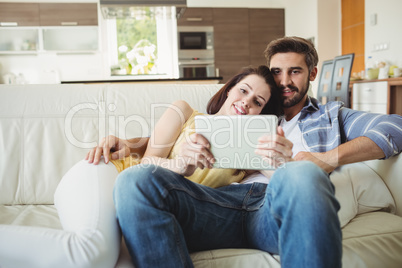 Happy couple using digital tablet while relaxing on sofa