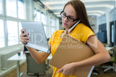 Female business executive using digital tablet and talking on mobile phone