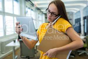 Female business executive using digital tablet and talking on mobile phone
