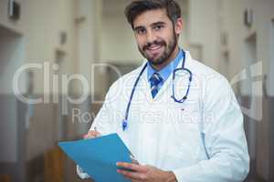Portrait of male doctor writing on clipboard in corridor