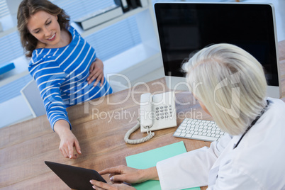 Doctor discussing with pregnant patient over digital tablet