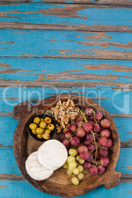 Cheese, grapes, olives and walnuts in wooden bowl