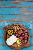 Cheese, grapes, olives and walnuts in wooden bowl