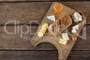 Variety of cheese, brown bread and knife on wooden board