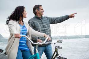 Happy couple on bicycle pointing at distance on beach