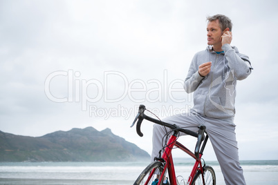 Man standing with bicycle listening music on headphones at beach