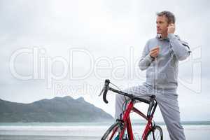 Man standing with bicycle listening music on headphones at beach