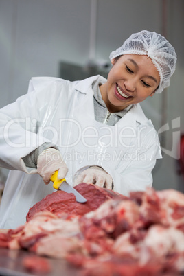 Female butcher cutting meat at meat factory