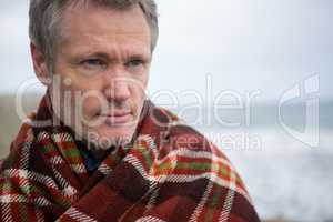 Thoughtful man wrapped in shawl at the beach