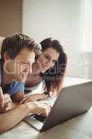 Happy couple using laptop on bed