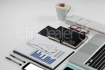 Laptop, coffee mug, smartphone, business graph and office desk tops