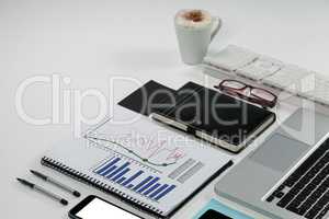 Laptop, coffee mug, smartphone, business graph and office desk tops