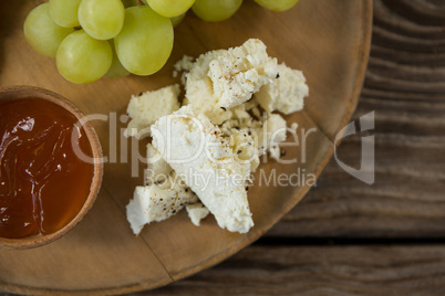 Cheese with grapes and sauce on wooden plate