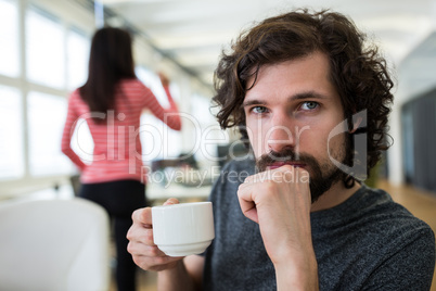 Male graphic designer holding coffee cup at desk