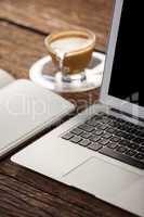 Cup of coffee with diary and laptop on wooden table
