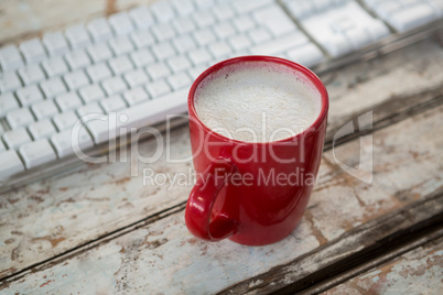 Cup of coffee beside keyboard on wooden table