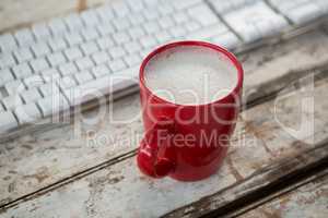 Cup of coffee beside keyboard on wooden table