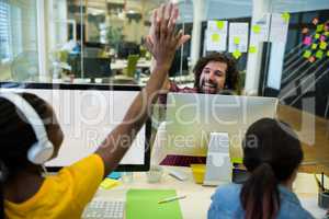 Team of business executives giving high five at desk