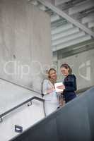 Businesswomen standing on staircase and using digital tablet