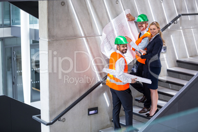 Businesswoman and architects standing on a staircase discussing with blueprint