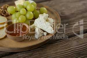 Cheese with grapes and sauce on wooden plate