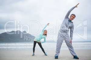 Couple performing stretching exercise on beach
