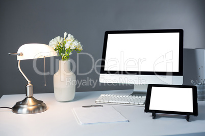 Desktop pc, digital tablet and table lamp with flower vase on table