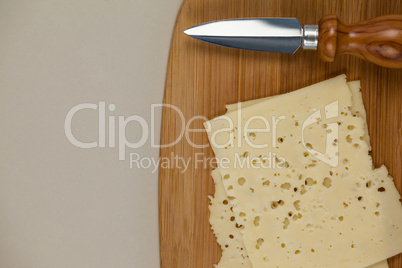 Slices of cheese with knife on chopping board