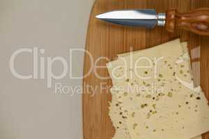 Slices of cheese with knife on chopping board