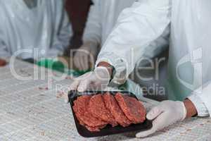 Mid section of butcher holding raw meat patties arranged in tray