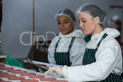 Female butchers maintaining records on clipboard