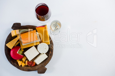 Glasses of wine with variety of cheese on wooden plate