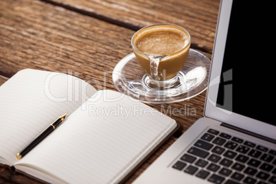 Cup of coffee with diary and laptop on wooden table