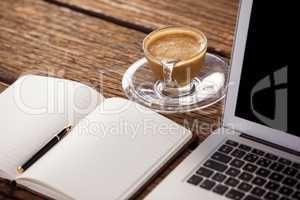 Cup of coffee with diary and laptop on wooden table