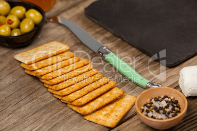 Bowl of green olives, biscuit and knife on wooden table