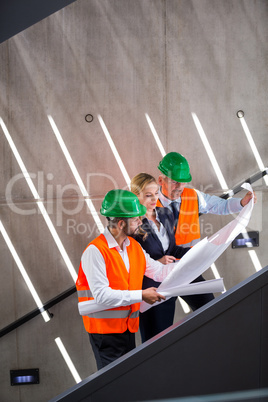 Businesswoman and architects standing on a staircase discussing with blueprint