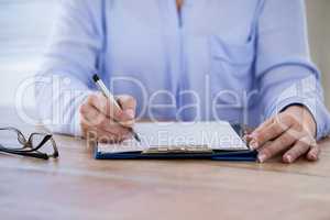 Mid section of doctor writing on clipboard