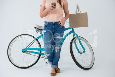 Woman with shopping bag and bicycle using mobile phone