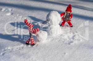 Two small wooden man in the scene of building a snowman among th